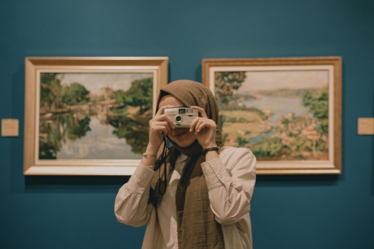 A woman with a headscarf captures art paintings in a gallery setting.